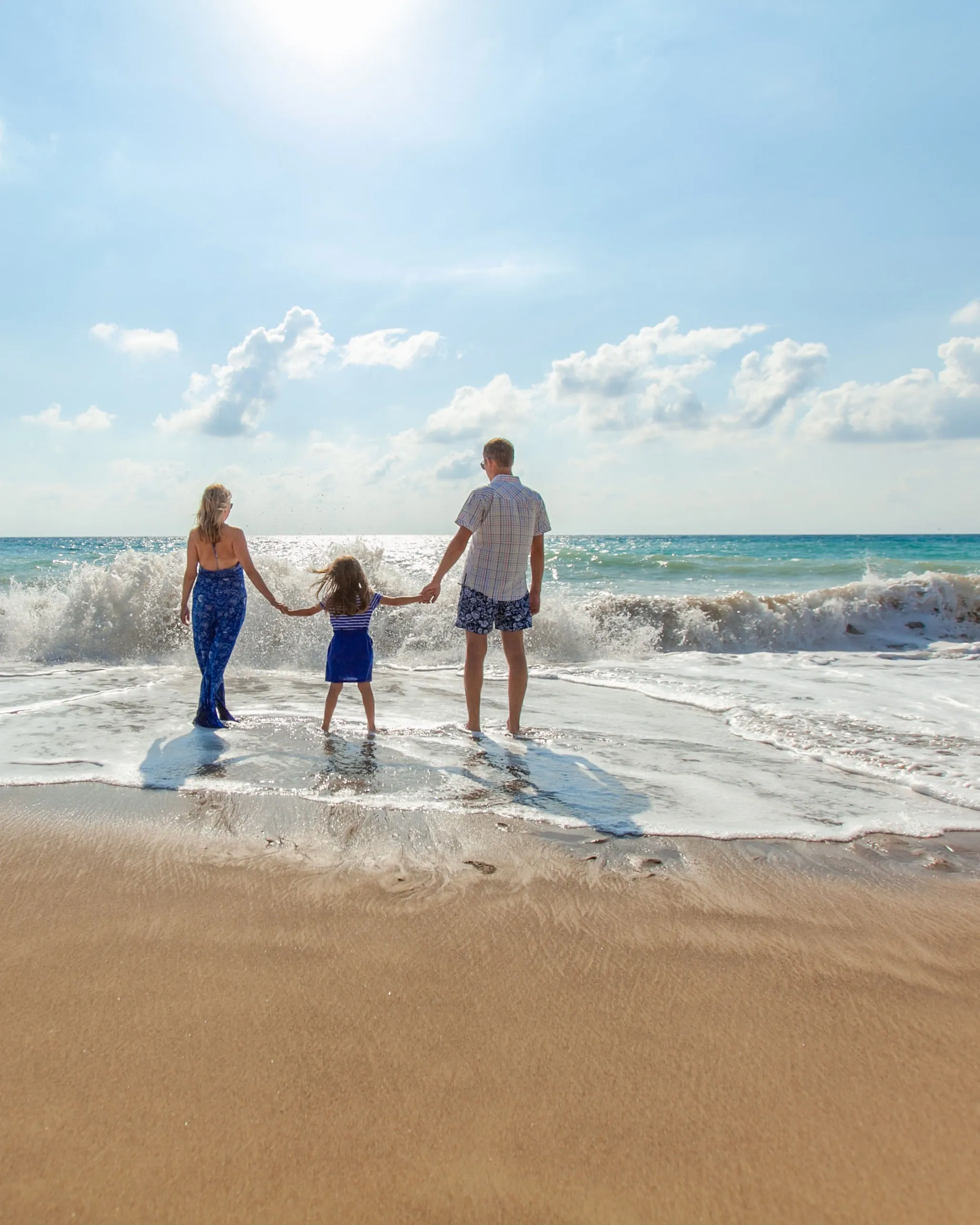 Eine Familie läuft vom Strand ins Meer, Hand in Hand.