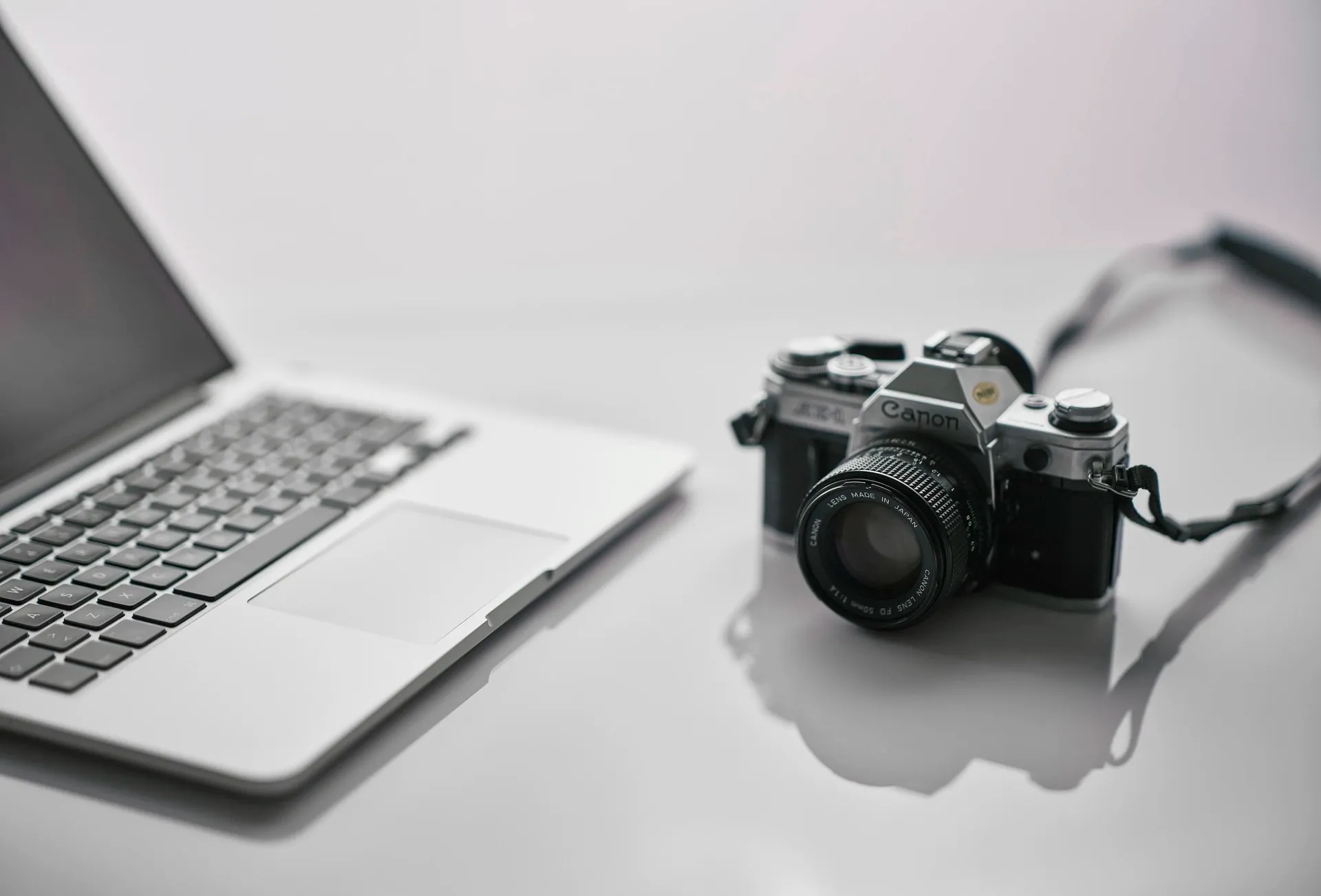 Ein silberner Laptop und eine silbern/schwarze Kamera von Canon auf weißem Hintergrund.