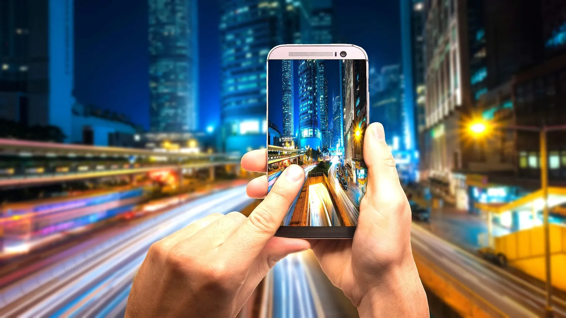 Ein silbernes Smartphone vor einer bunten langzeitbelichteten Infrastruktur einer Stadt.
